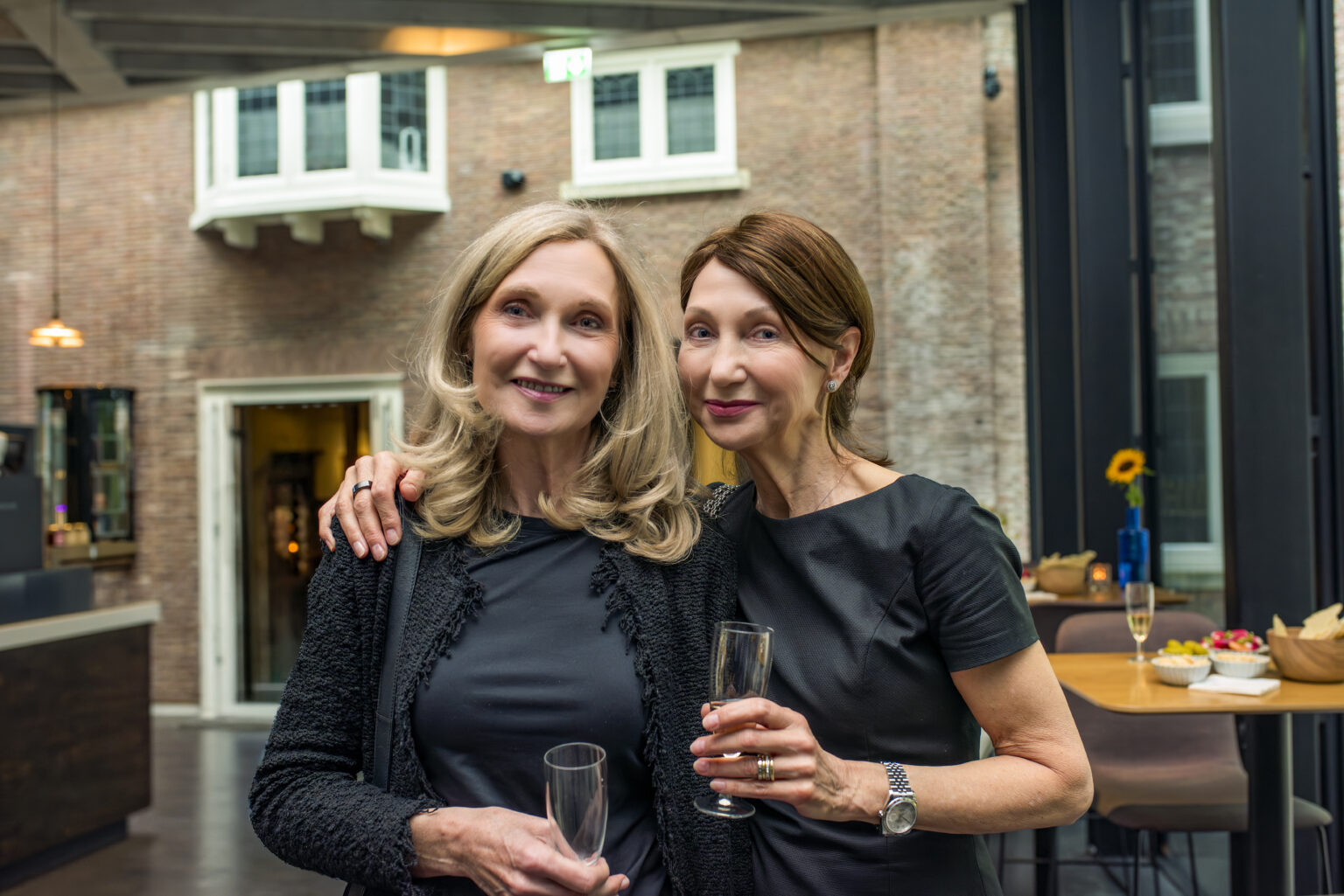 Two women stand arm in arm with champagne glasses at the celebration.