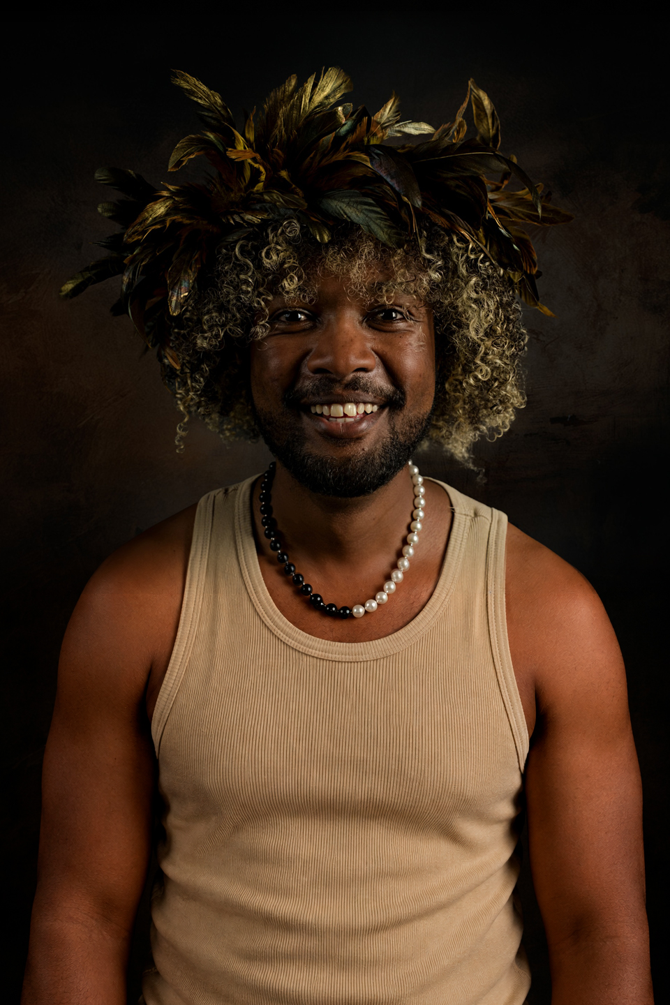 Smiling editorial portrait wearing a feather crown and a black-and-white pearl necklace