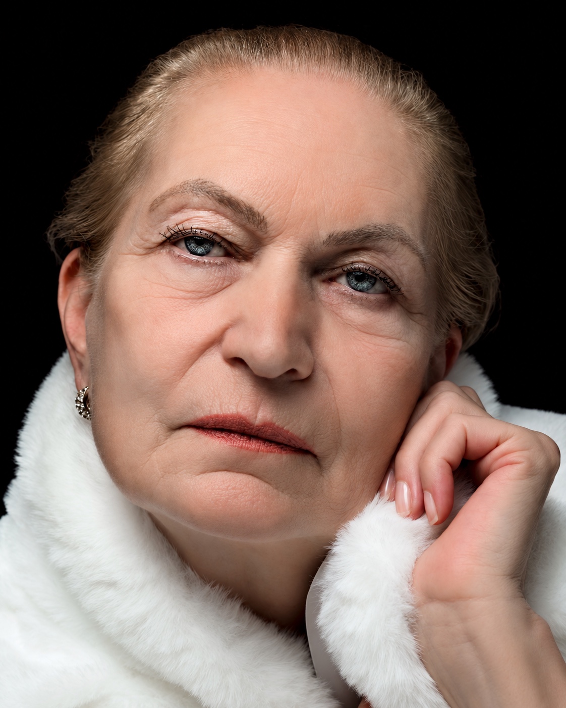Close editorial beauty portrait of a woman in white, holding the collar beside her face